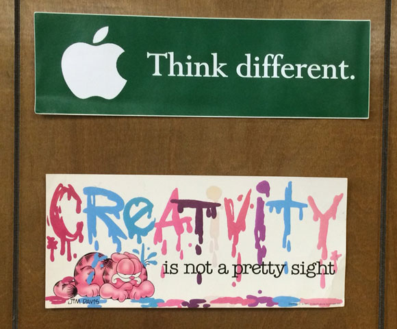 Two bumper stickers on the 1970s-era wood paneling in my office.